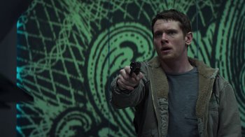 Movie still from “Money Monster” (2016), directed by Jodie Foster – A man holding a gun in front of a green wall; Medium shot, Low angle