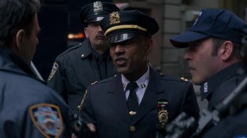 Movie still from “Money Monster” (2016), directed by Jodie Foster – A man in a police officer's uniform is standing in front of other men; Close Up shot, Over the shoulder angle