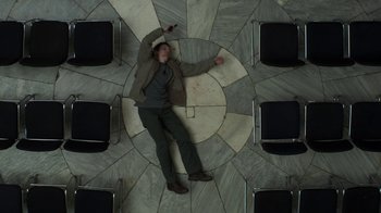 Movie still from “Money Monster” (2016), directed by Jodie Foster – A man laying on the floor in a circle of chairs; Wide shot, Overhead angle