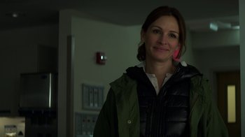 Movie still from “Money Monster” (2016), directed by Jodie Foster – A woman in a green jacket is smiling for the camera; Close Up shot, Over the shoulder angle