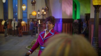 Movie still from “Monster High: The Movie” (2022), directed by Todd Holland – A woman standing in front of other people in a room; Medium shot, Over the shoulder angle