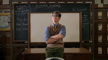 Movie still from “Monster High: The Movie” (2022), directed by Todd Holland – A man standing in front of a chalkboard with his arms crossed; Medium shot, Over the shoulder angle