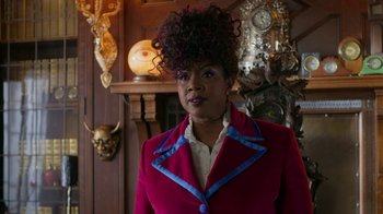 Movie still from “Monster High: The Movie” (2022), directed by Todd Holland – A woman in a red and blue jacket standing in front of a fireplace; Medium shot, Low angle