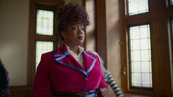 Movie still from “Monster High: The Movie” (2022), directed by Todd Holland – A woman in a pink jacket and a blue and white striped tie; Medium shot, Low angle