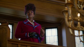 Movie still from “Monster High: The Movie” (2022), directed by Todd Holland – A woman in a red jacket is standing in front of a window; Medium shot, Low angle