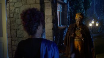 Movie still from “Monster High: The Movie” (2022), directed by Todd Holland – A woman in a blue dress and a man in a yellow suit stand in front of a brick building; Medium shot, Over the shoulder angle