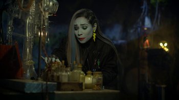 Movie still from “Monster High: The Movie” (2022), directed by Todd Holland – A woman in black shirt and yellow earrings looking down; Close Up shot, High angle