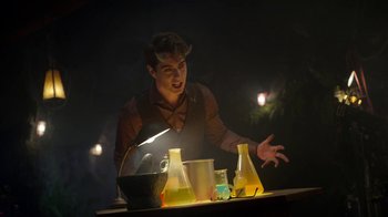Movie still from “Monster High: The Movie” (2022), directed by Todd Holland – A man in a brown shirt is standing in front of a table; Medium shot, Over the shoulder angle