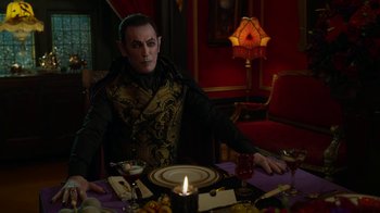 Movie still from “Monster High: The Movie” (2022), directed by Todd Holland – A man sitting at a table with a plate of food; Medium shot, Over the shoulder angle