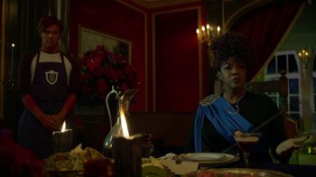 Movie still from “Monster High: The Movie” (2022), directed by Todd Holland – A woman sitting at a table with a vase of flowers in front of her; Medium shot, Over the shoulder angle