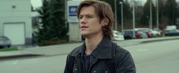 Movie still from “Monster Trucks” (2016), directed by Chris Wedge – A man with long brown hair standing on the side of the street; Close Up shot, Over the shoulder angle