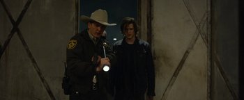 Movie still from “Monster Trucks” (2016), directed by Chris Wedge – A man in a cowboy hat is holding a flashlight and standing next to another man; Medium shot, Over the shoulder angle