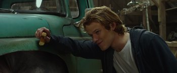 Movie still from “Monster Trucks” (2016), directed by Chris Wedge – A man leaning against the side of an old green truck; Close Up shot, Over the shoulder angle