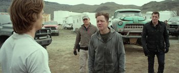 Movie still from “Monster Trucks” (2016), directed by Chris Wedge – Two men standing next to each other on a dirt field; Medium shot, Over the shoulder angle