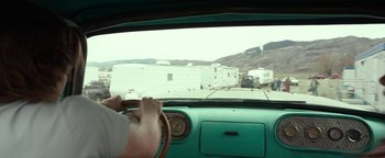 A man driving a car with a trailer in the background