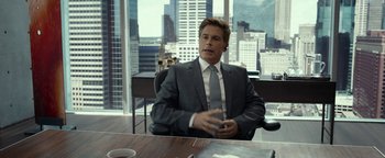 A man sitting at a table in a suit and tie in front of a window