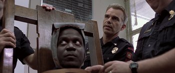 Movie still from “Monster's Ball” (2001), directed by Marc Forster – A police officer holding a wooden cross over a man's head; Close Up shot, Over the shoulder angle