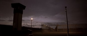 Movie still from “Monster's Ball” (2001), directed by Marc Forster – A car parked in a parking lot next to barbed wire fence; Extreme Wide shot, Low angle