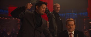 Movie still from “Mortdecai” (2015), directed by David Koepp – A man holding a knife in front of another man in a suit; Medium shot, Over the shoulder angle