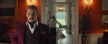 Movie still from “Mortdecai” (2015), directed by David Koepp – A man in a suit and a woman in a white dress in a room; Medium shot, Over the shoulder angle