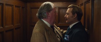 Movie still from “Mortdecai” (2015), directed by David Koepp – A man and a man in a suit face each other in front of a wooden wall; Close Up shot, Over the shoulder angle