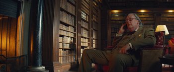 Movie still from “Mortdecai” (2015), directed by David Koepp – A man sitting in front of a book shelf filled with lots of books; Medium shot, Low angle