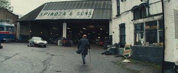 Movie still from “Mortdecai” (2015), directed by David Koepp – A man walking down a street in front of a building; Wide shot, Low angle