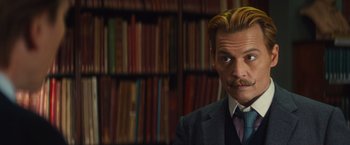 Movie still from “Mortdecai” (2015), directed by David Koepp – A man in a suit and tie in front of bookshelves; Close Up shot, Over the shoulder angle