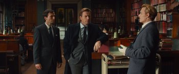 Movie still from “Mortdecai” (2015), directed by David Koepp – A man standing next to another man in a library; Medium shot, Low angle