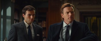 Movie still from “Mortdecai” (2015), directed by David Koepp – A man in a suit and tie standing next to another man in a suit and tie; Close Up shot, Over the shoulder angle