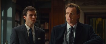 Movie still from “Mortdecai” (2015), directed by David Koepp – A man in a suit and tie standing next to another man in a suit and tie; Close Up shot, Over the shoulder angle