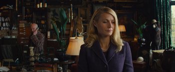 Movie still from “Mortdecai” (2015), directed by David Koepp – A woman in a purple jacket standing next to a lamp; Medium shot, Over the shoulder angle