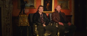 Movie still from “Mortdecai” (2015), directed by David Koepp – Two men sitting in chairs in front of a painting; Medium shot, Low angle