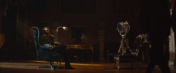 Movie still from “Mortdecai” (2015), directed by David Koepp – A woman sitting in a chair in front of an old fashioned fan; Wide shot, Low angle