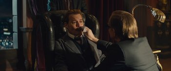 Movie still from “Mortdecai” (2015), directed by David Koepp – A man sitting in a chair while a woman puts something in his mouth; Medium shot, Over the shoulder angle
