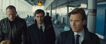 Movie still from “Mortdecai” (2015), directed by David Koepp – Two men are standing in an airport waiting area; Close Up shot, Over the shoulder angle