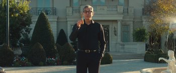 Movie still from “Mortdecai” (2015), directed by David Koepp – A man in a black shirt and black pants holding a wooden stick; Medium shot, Low angle