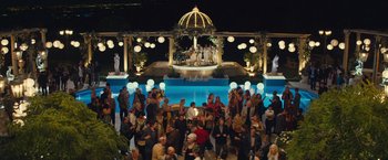 Movie still from “Mortdecai” (2015), directed by David Koepp – A group of people standing around a pool at night; Extreme Wide shot, High angle