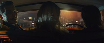 Movie still from “Mortdecai” (2015), directed by David Koepp – A woman sitting in the back seat of a car at night; Medium shot, Over the shoulder angle