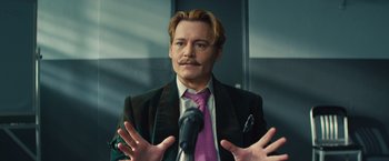 Movie still from “Mortdecai” (2015), directed by David Koepp – A man in a suit and tie holding a microphone; Close Up shot, Low angle