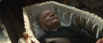 Movie still from “Mortdecai” (2015), directed by David Koepp – An older man in a suit and tie laying in a casket; Close Up shot, High angle