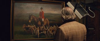 Movie still from “Mortdecai” (2015), directed by David Koepp – A man standing in front of a painting of a dog and a horse; Medium shot, Over the shoulder angle