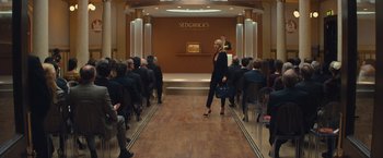Movie still from “Mortdecai” (2015), directed by David Koepp – A woman standing in front of an audience on a stage; Wide shot, High angle