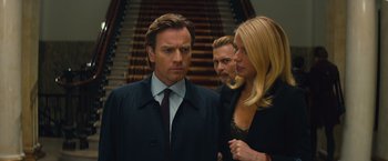Movie still from “Mortdecai” (2015), directed by David Koepp – Two men and a woman standing next to each other in front of a staircase; Close Up shot, Over the shoulder angle