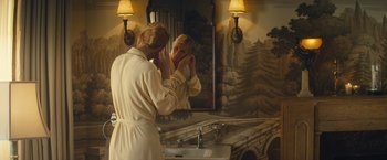 Movie still from “Mortdecai” (2015), directed by David Koepp – A woman in a bathrobe looking in the mirror in front of a bathroom sink; Medium shot, Over the shoulder angle
