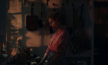 Movie still from “Mothering Sunday” (2021), directed by Eva Husson – A woman standing in front of a bunch of wall hangers; Medium shot, Over the shoulder angle