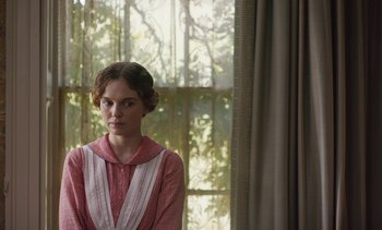 Movie still from “Mothering Sunday” (2021), directed by Eva Husson – A woman in a red and white dress standing in front of a window; Medium shot, Over the shoulder angle