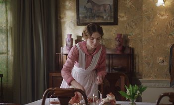 Movie still from “Mothering Sunday” (2021), directed by Eva Husson – A woman standing at a dining room table; Medium shot, Over the shoulder angle