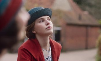 Movie still from “Mothering Sunday” (2021), directed by Eva Husson – A young woman wearing a hat and a red jacket; Close Up shot, Over the shoulder angle