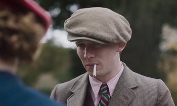 Movie still from “Mothering Sunday” (2021), directed by Eva Husson – A man in a suit and hat smoking a cigarette; Close Up shot, Over the shoulder angle